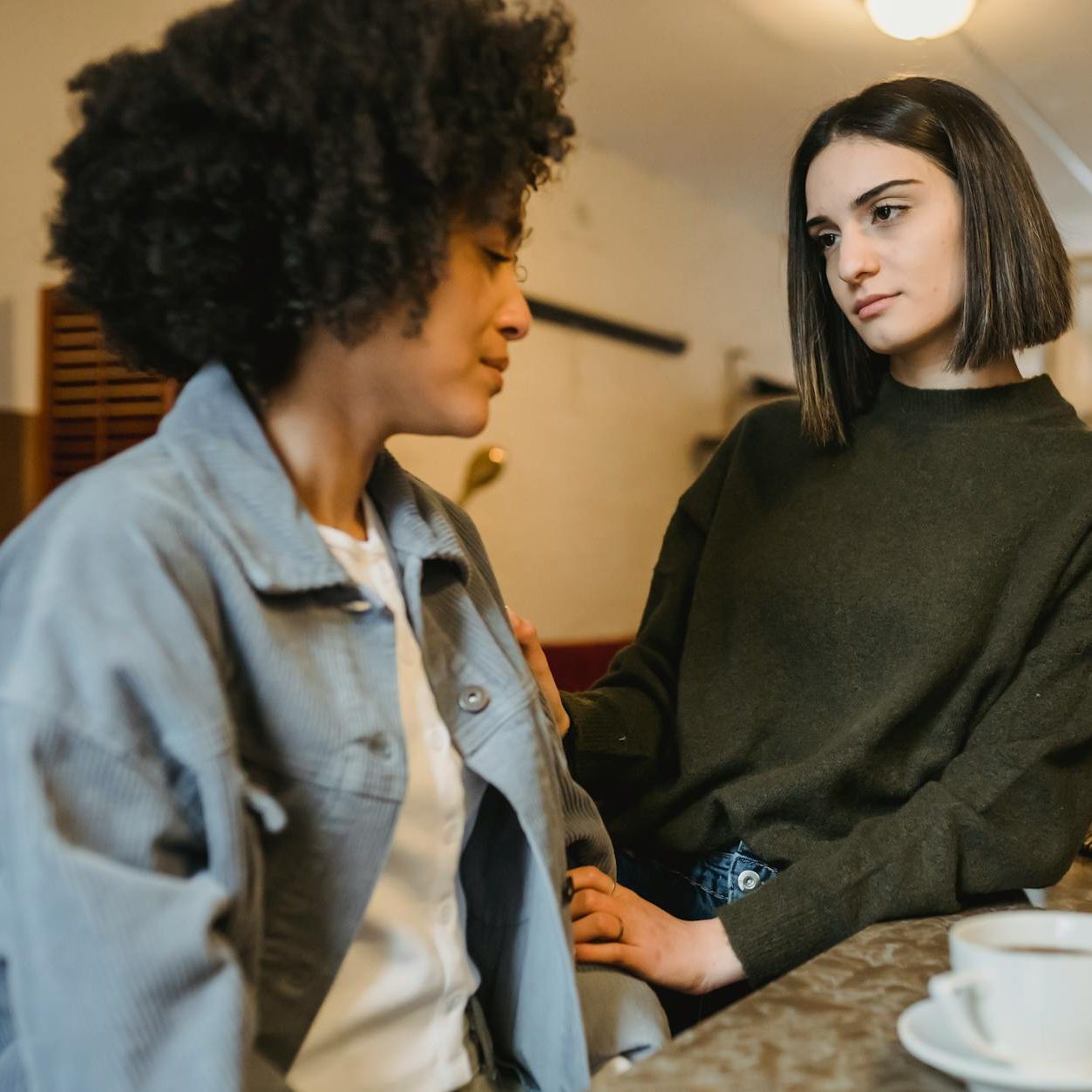 One person in a green sweater looks with concern at another person in a blue jacket who looks sad.
