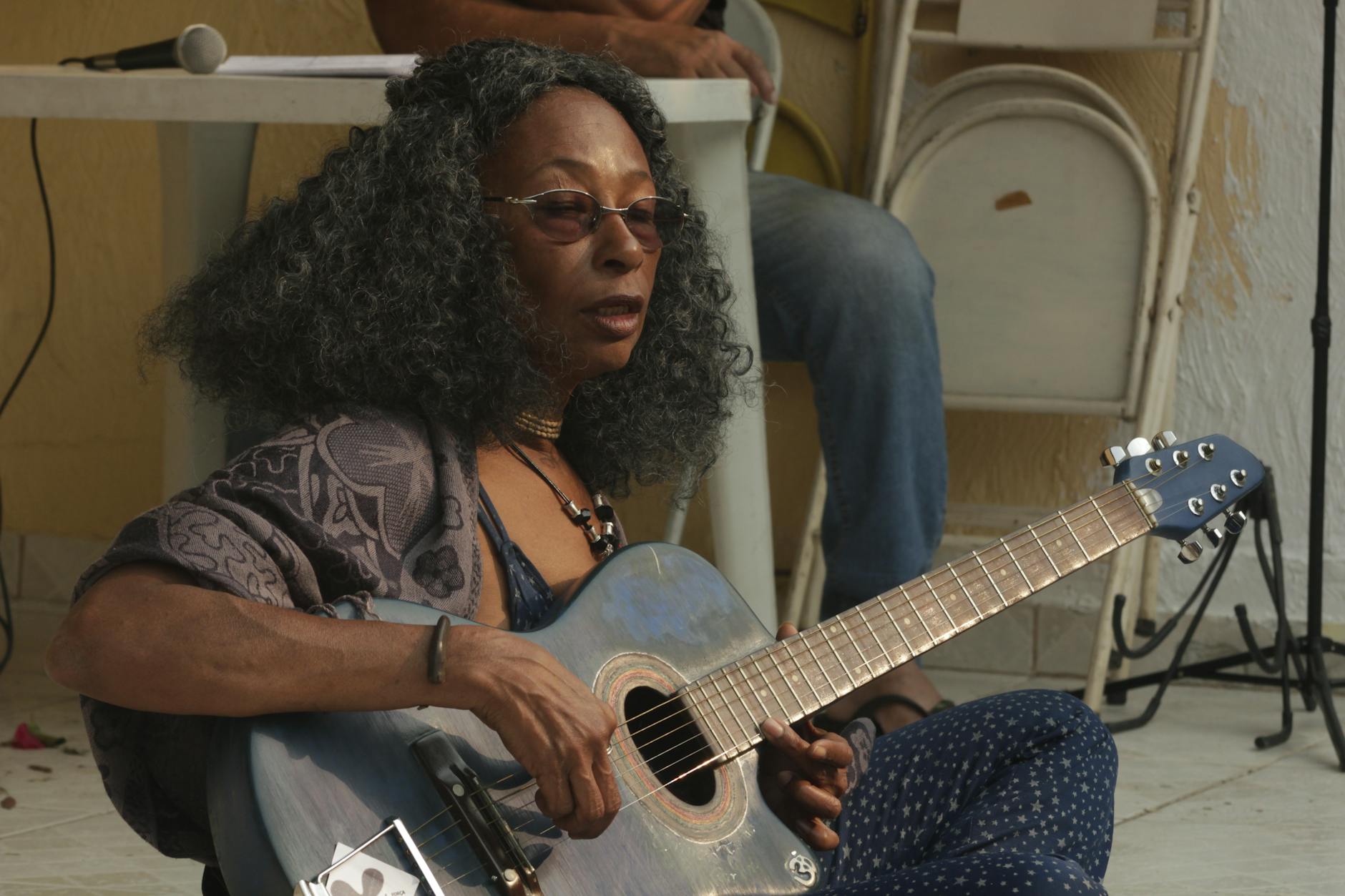 A woman with long hair and tinted glasses playing guitar.